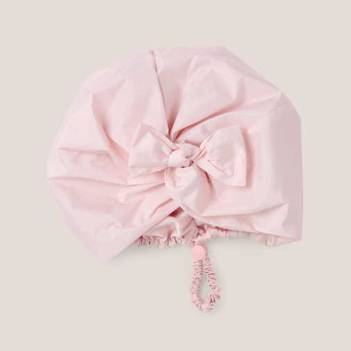 A light pink waterproof rain cover with a large decorative bow at the top center and a matching drawstring cord, shown on a solid light beige background.