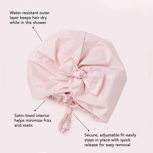 A light pink shower cap cover with text callouts explaining its water-resistant outer layer, satin-lined interior, and adjustable elastic closure on a pale pink background.
