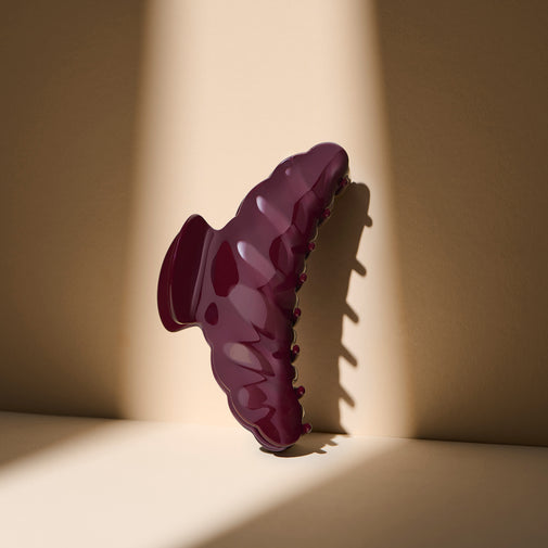 The Hair Edit Bordeaux Claw Clip standing up against a beige wall