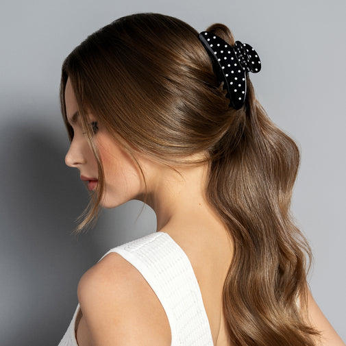 Woman with styled hair featuring a black polka dot hair accessory on a gray background