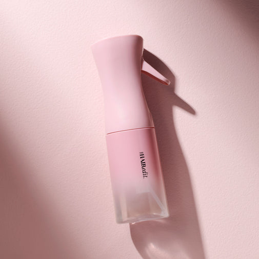 A pink spray bottle with a clear lower section and black vertical text reading 'THE HAIR EDIT', photographed on a soft pink background with a strong shadow.