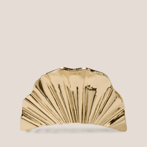 A metallic gold claw clip with a scalloped, fan-like pleated design, shown against a solid light beige background.