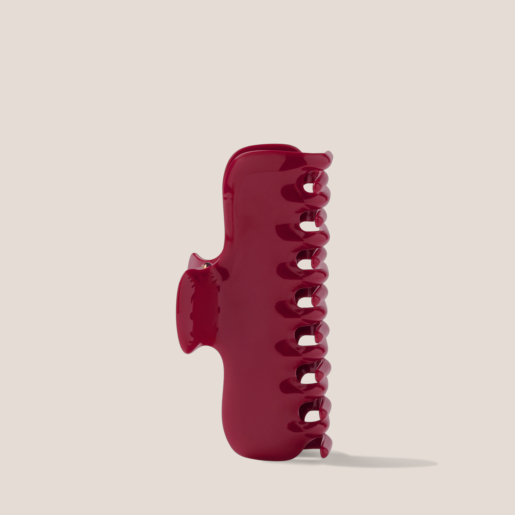 A glossy dark red hair claw clip standing upright on a light beige background.