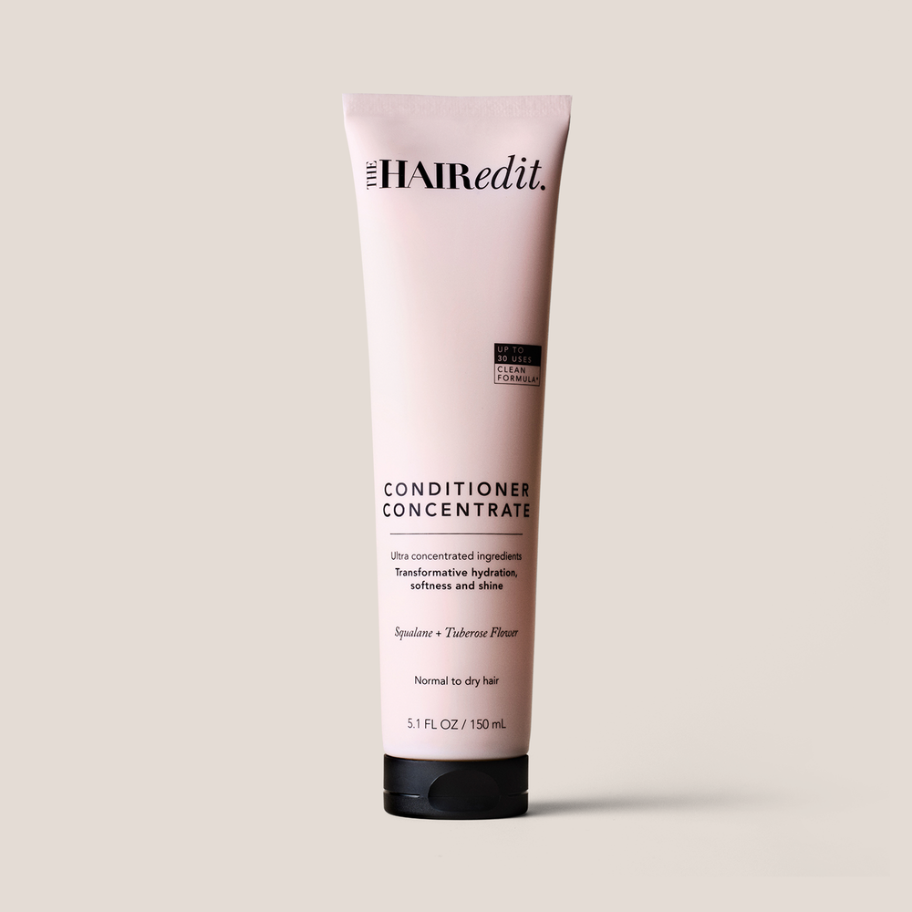 A 5.1 fl oz squeeze tube of The Hair Edit Conditioner Concentrate, featuring a pale pink body and a black cap, set against a solid light beige background.1
