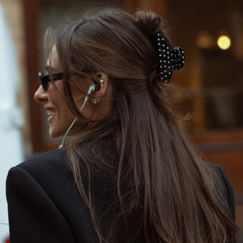 Woman with long hair tied back wearing glasses and a black blazer.3