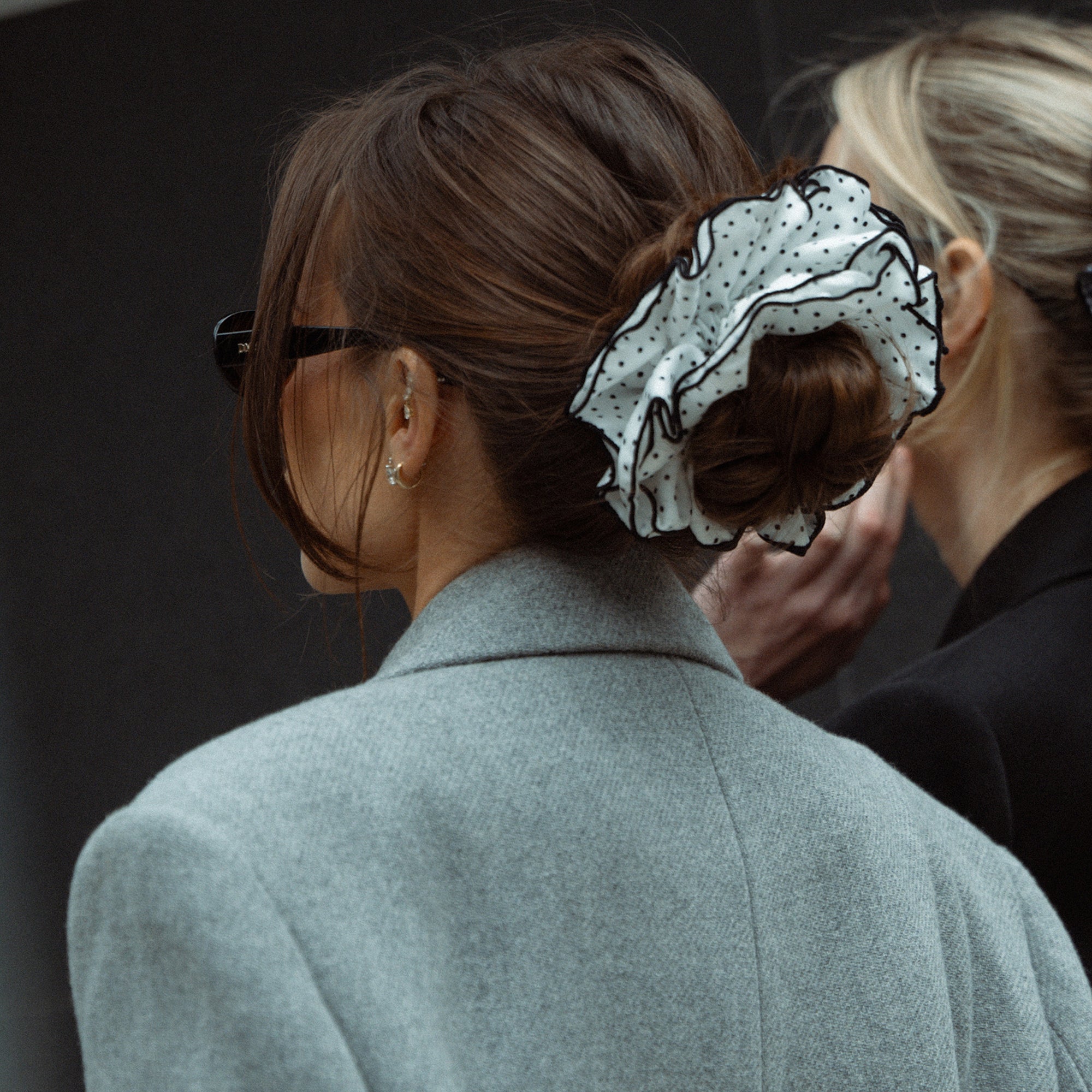 Person wearing a gray coat with a decorative hair scrunchie on a dark background3