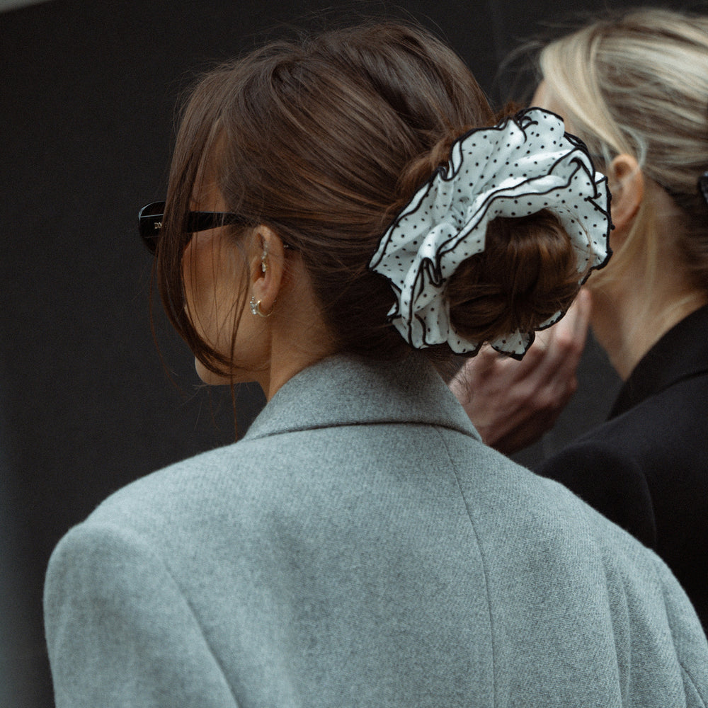 Person wearing a gray coat with a decorative hair scrunchie on a dark background3