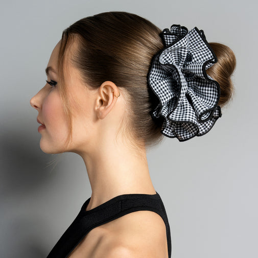 A woman in profile wearing a large black and white gingham ruffled hair scrunchie, styled in a low bun.