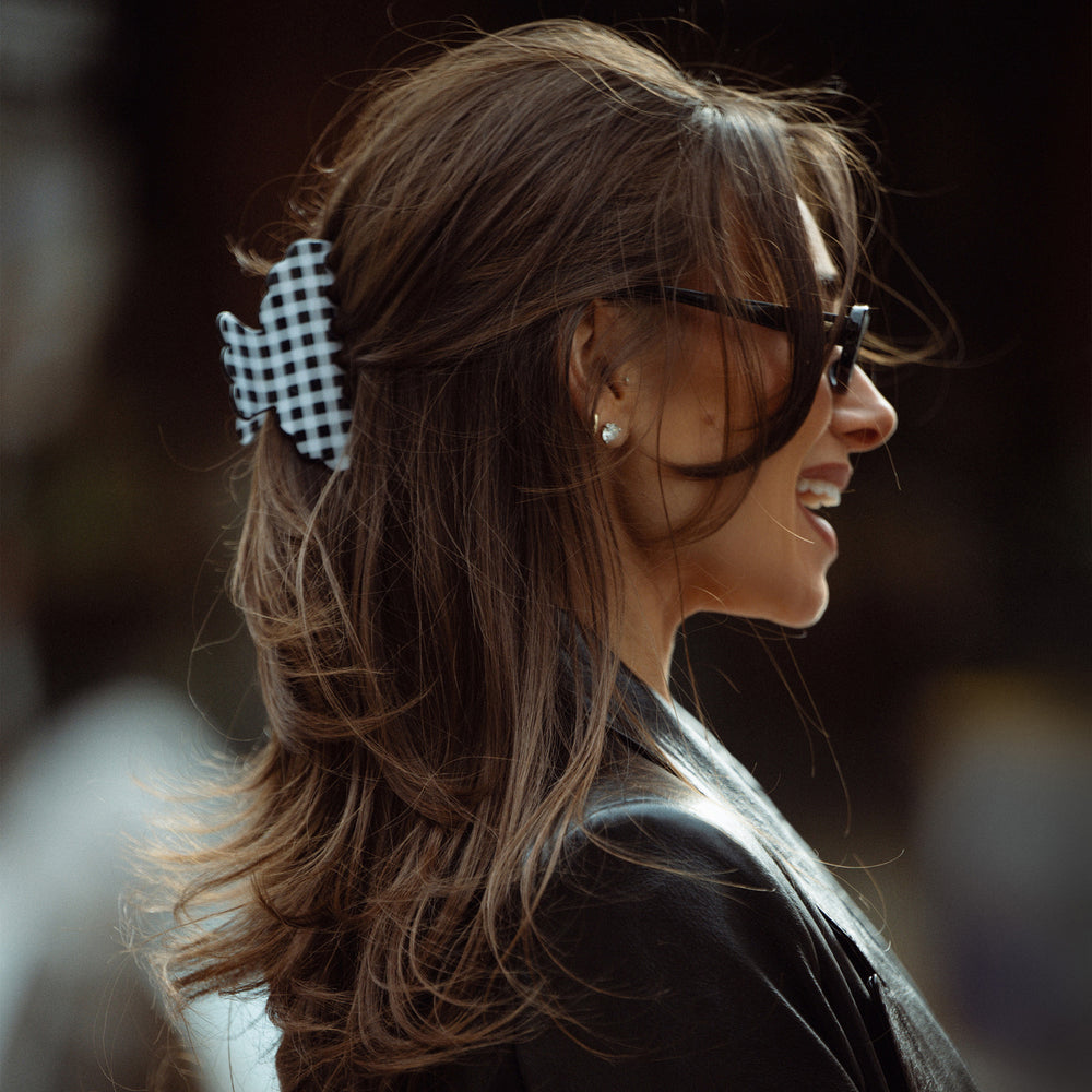 A woman in profile wearing a black and white gingham bow hair clip, styled with brown hair, black sunglasses, and a black leather jacket.3