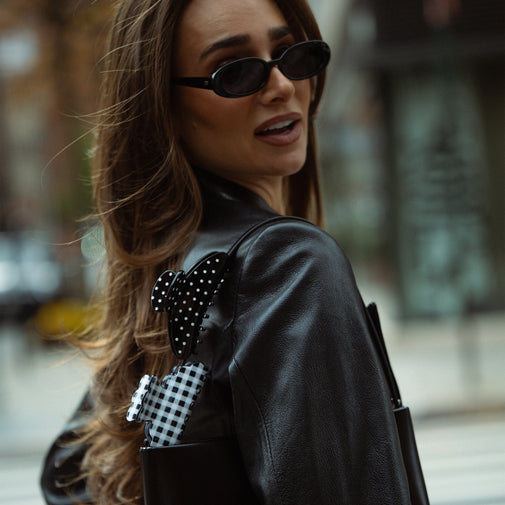 Woman wearing sunglasses and a black leather jacket with decorative elements on a blurred street background
