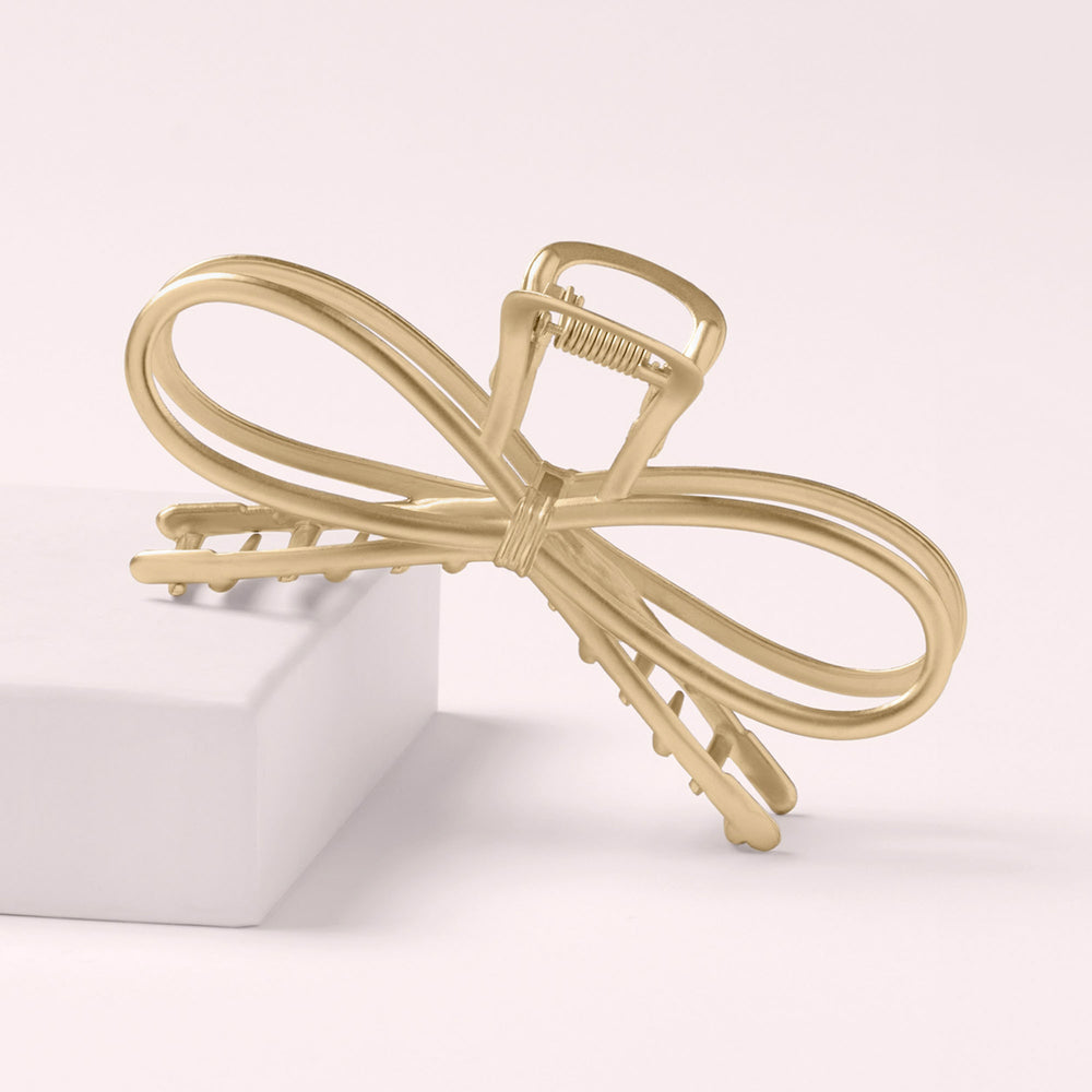 The Hair Edit Gilded Festive Bow Claw Clip leaning on a pink box with a light pink background4