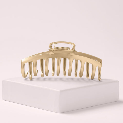The Hair Edit Gilded Timeless Claw Clip leaning on a pink box with a light pink background