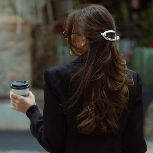 Woman with long brown hair holding a coffee cup, wearing a black coat.