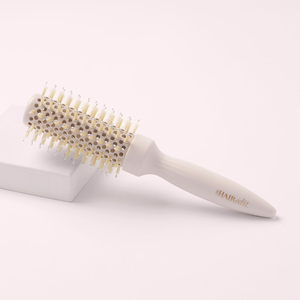 a round hairbrush with a cream-colored handle and bristles, set against a pink box on a pink background4