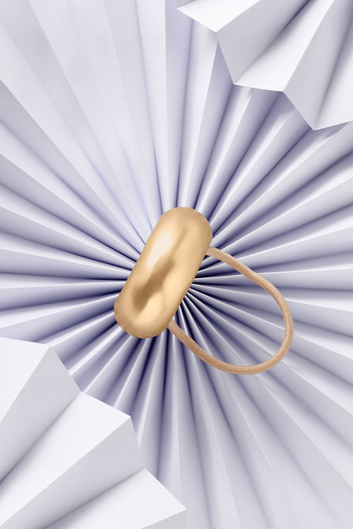 The Hair Edit Brilliant Cuff Arched Gold Metal Hair Tie on blue paper 