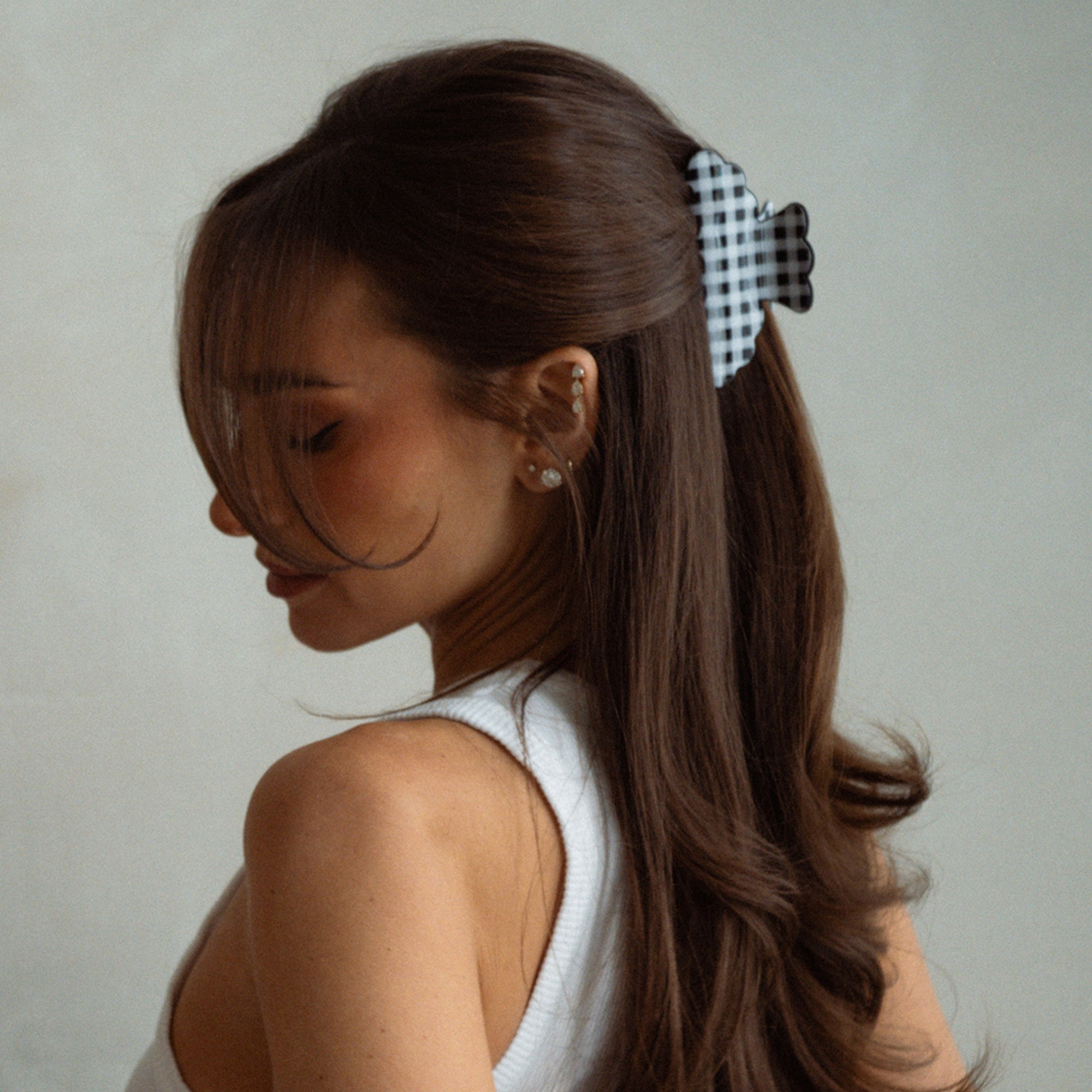 A woman with long brown hair wearing a black and white gingham check hair claw clip, shown in profile against a neutral light gray background.6