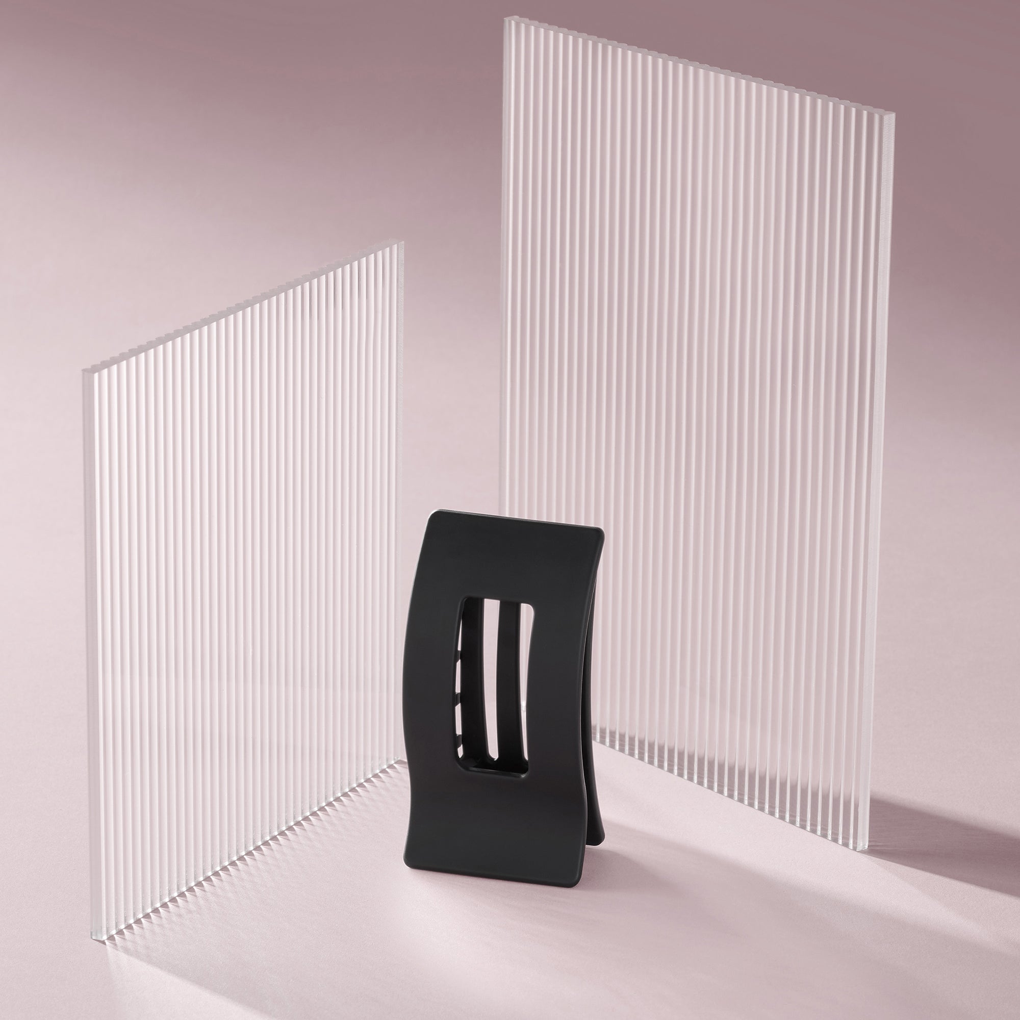 A black rectangle flat lay claw clip standing up, displayed in front of two tall white slatted panels on a soft pink studio background.6
