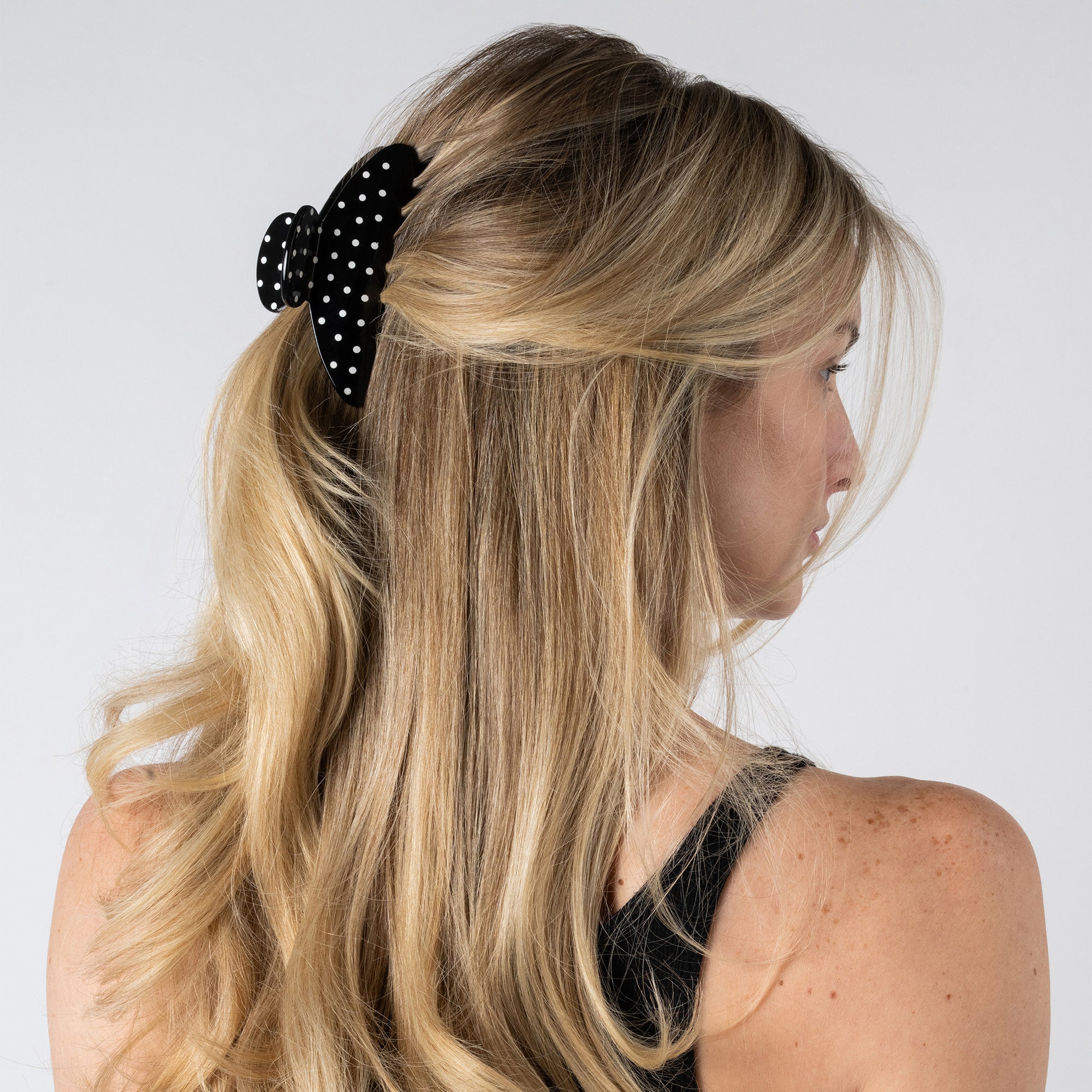 Woman with long blonde hair wearing a black polka dot hair clip on a white background7