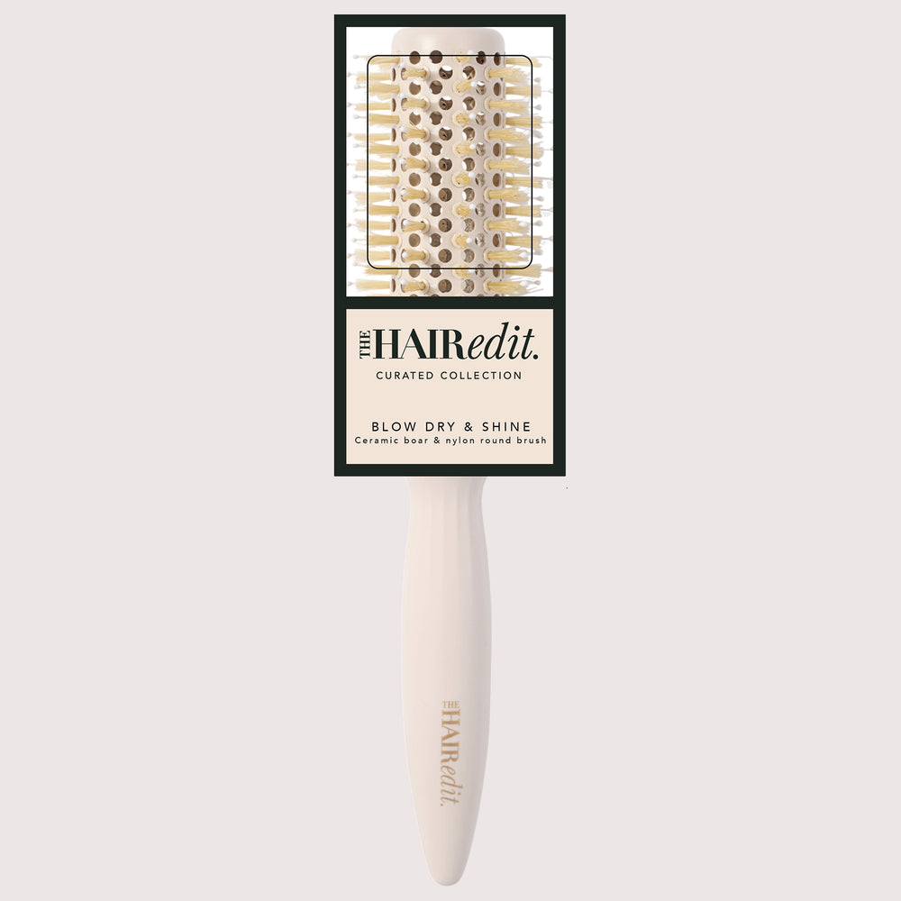 The Hair Edit Blow Dry & Shine ceramic brush with a cream-colored handle and gold-toned bristles, shown with its original black and cream packaging card against a light gray background.7