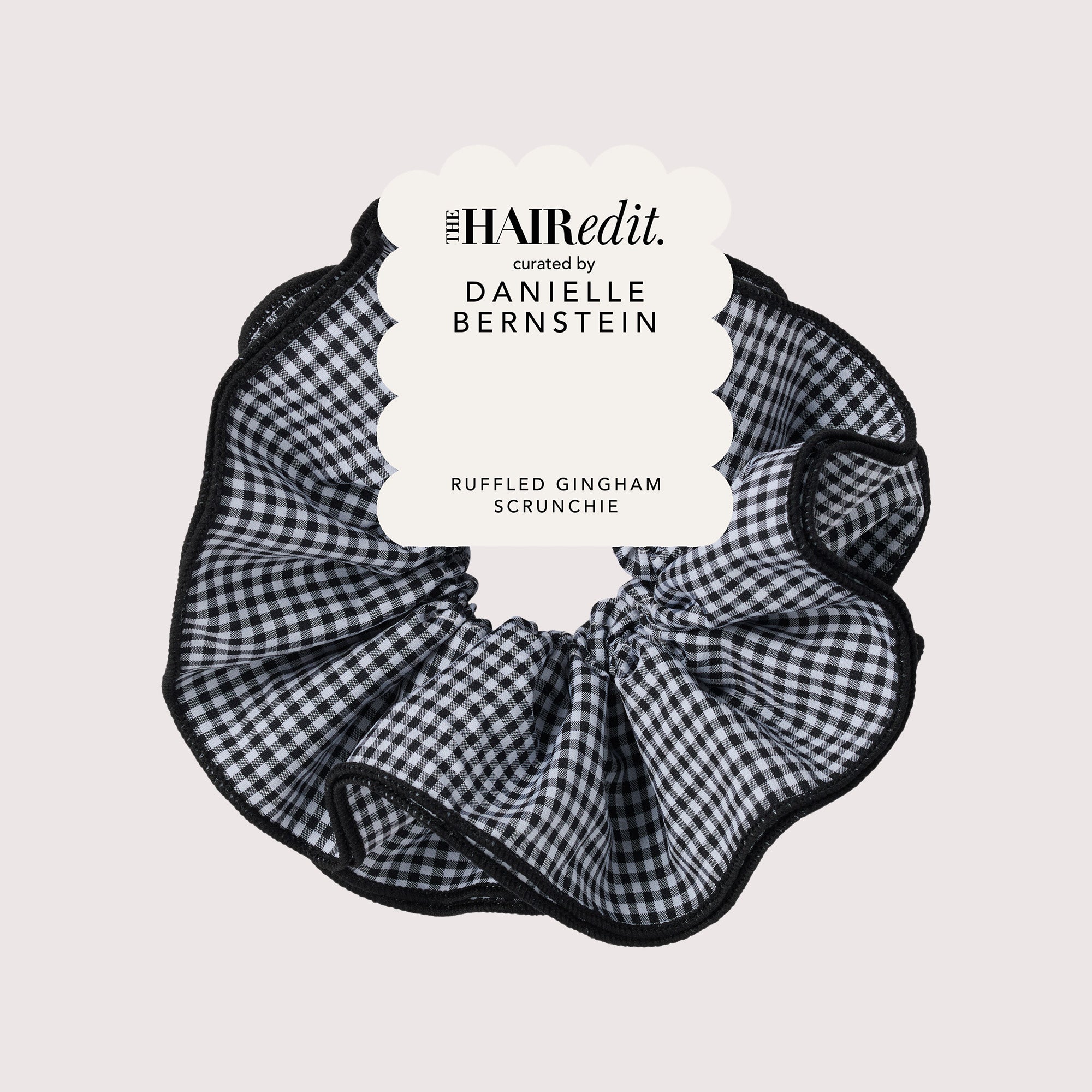 A black and white gingham ruffled scrunchie with a black lace trim, featuring a white paper label overlay that reads 'THE HAIRedit. curated by DANIELLE BERNSTEIN' and 'RUFFLED GINGHAM SCRUNCHIE'.10