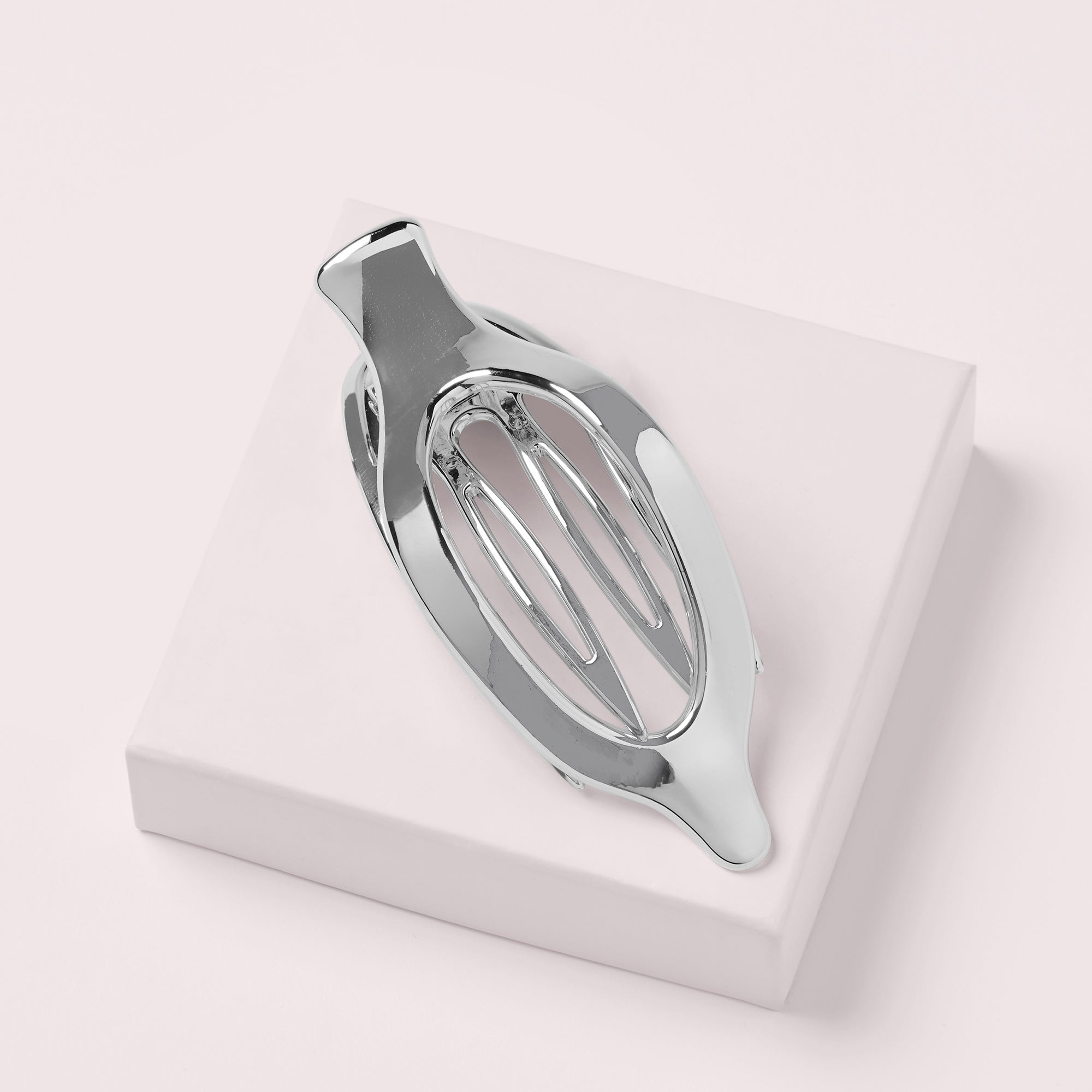 A polished silver metal hair claw clip displayed on a a pink box with a light pink background8