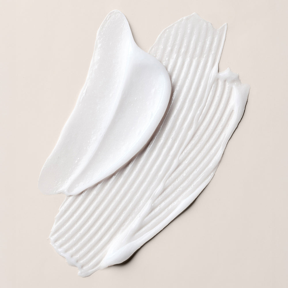 A close-up of a thick, creamy white cream swatch of the conditioner concentrate, showing both a smooth texture and a ribbed, whipped consistency, set against a solid light beige background.8