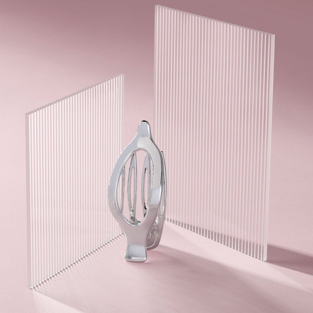 A polished silver metallic flat lay claw clip stands in the center between two tall, translucent white slatted panels on a soft pink studio background.9