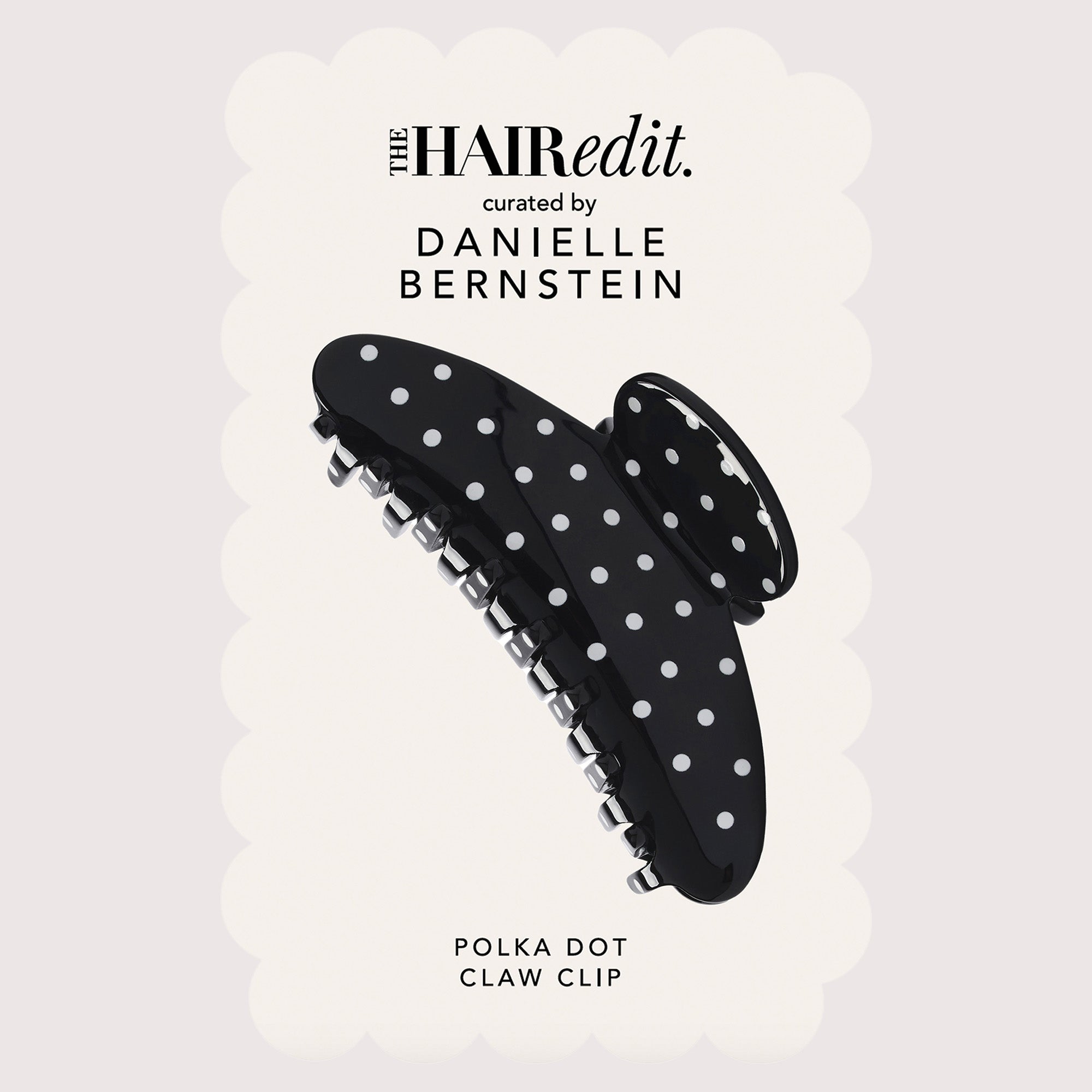 A black claw clip with white polka dots, shown against a light cream scalloped background with text reading 'the HAIRedit. curated by DANIELLE BERNSTEIN' and 'POLKA DOT CLAW CLIP'.10
