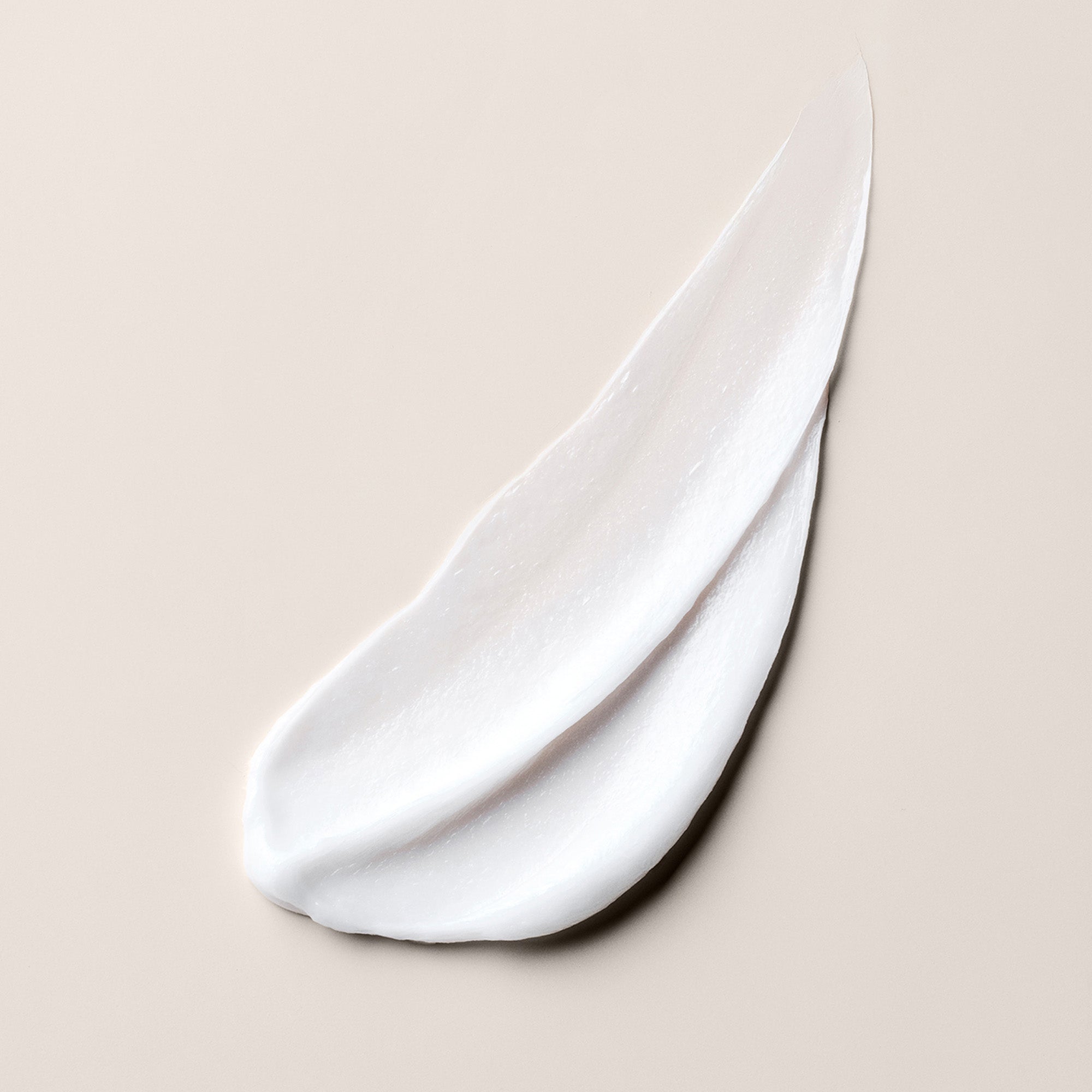 A thick, creamy white product smear of the hair mask on a warm beige background.9