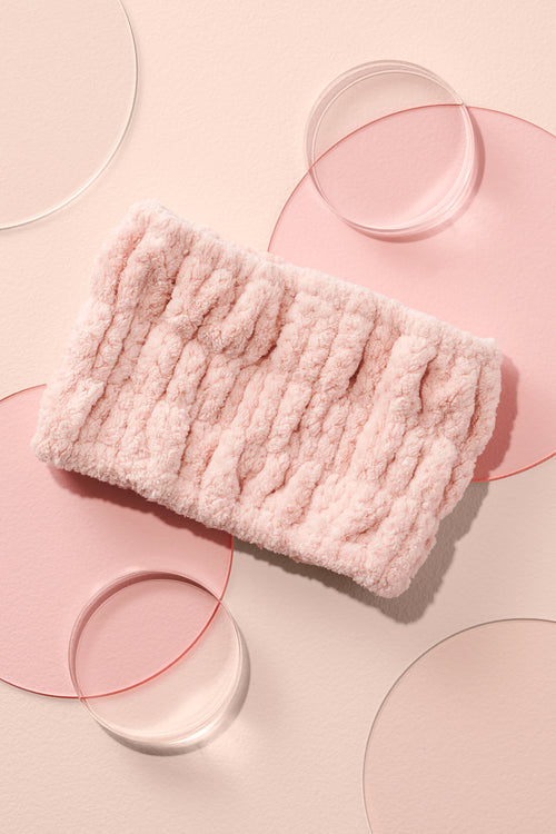 The Hair Edit Microfiber Spa Headband in a lifestyle shot with pink background and clear circles