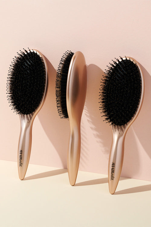 The Hair Edit Finish + Shine Boar Bristle Gold Hair Brushes displayed against pink backdrop