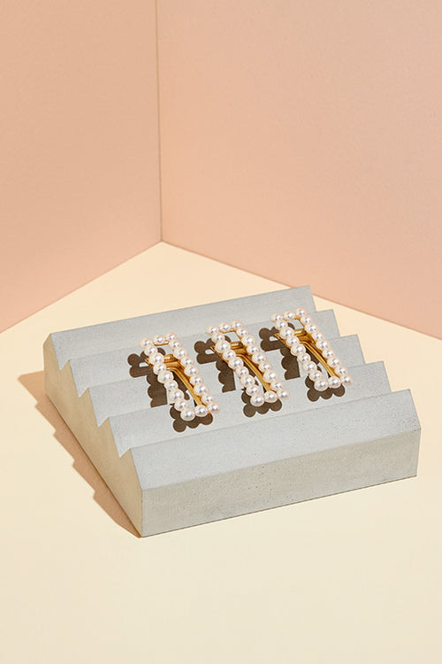 Three of The Hair Edit's Pearl Square Gold Jeweled Clip Hair Accessories in a row on cement block display