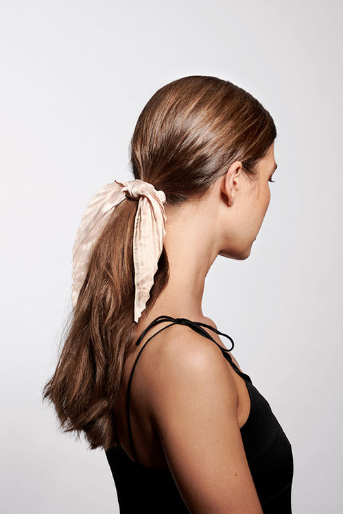 The Hair Edit cream colored pleated ribbon scrunchie hair tie worn by long haired brunette model with ponytail